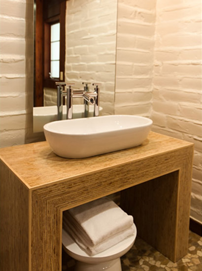 Bathroom sink resting up a wooden platform with mirror, towels and stool.