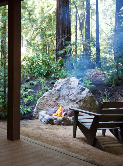Private view of a soaring redwood grove, framed by a sheltering porch and fire pit within view of forest greenery and tall tree trunks.