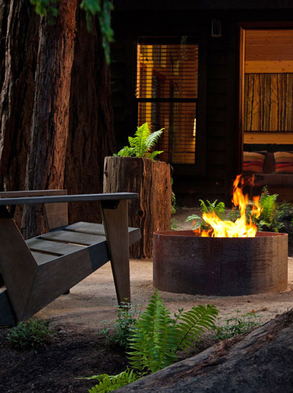 Exterior view of cabin with fire pit, chair and trees.