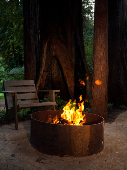private outdoor wood-stocked firepit with chair in wooded area.
