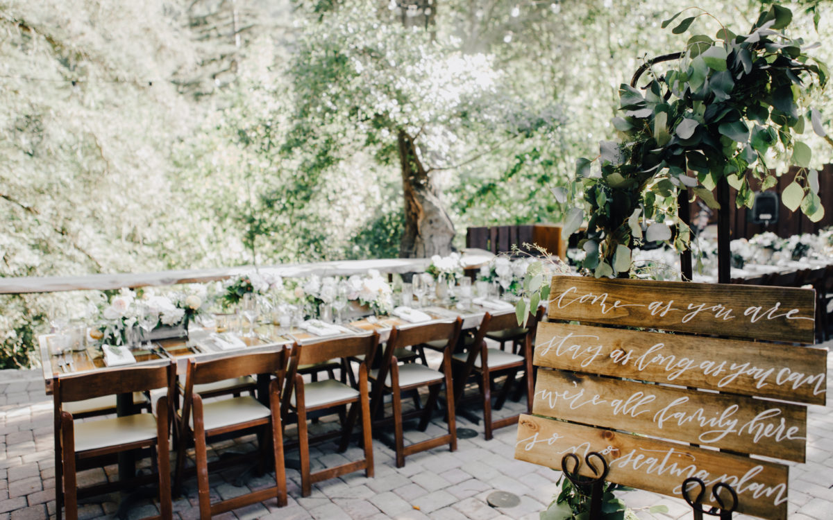 Table set for wedding reception meal on elevated platform with forest in the background.