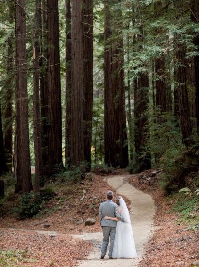 Bride and groom standing on a walking trail and embracing one another while gazing into the majestic forest.